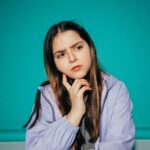 A young girl pondering deeply against a vibrant teal background.