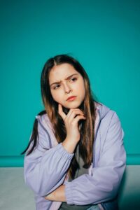 A young girl pondering deeply against a vibrant teal background.