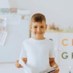 Cheerful boy holding a book in a bright classroom setting. Perfect for education themes.