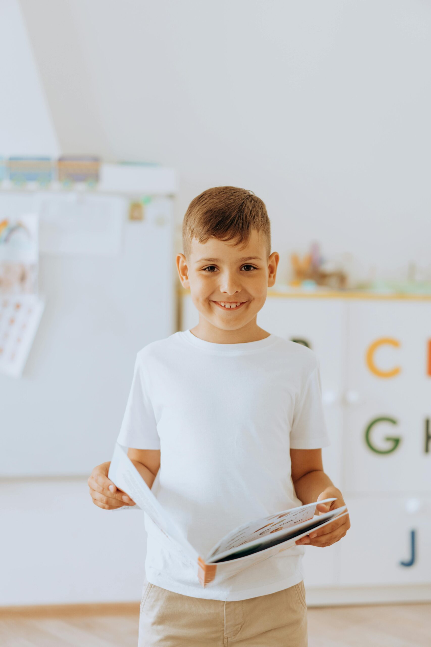 Cheerful boy holding a book in a bright classroom setting. Perfect for education themes.