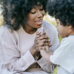 A mother and daughter with afro hair holding hands and smiling in a park setting.