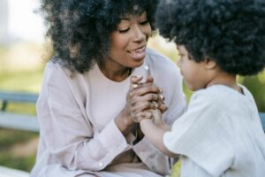 A mother and daughter with afro hair holding hands and smiling in a park setting.